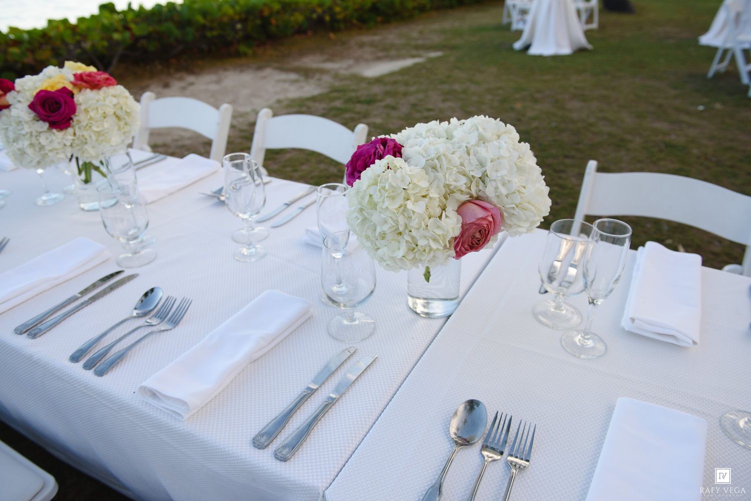 Elegant outdoor wedding reception table set with white linens, floral centerpieces, and glassware.