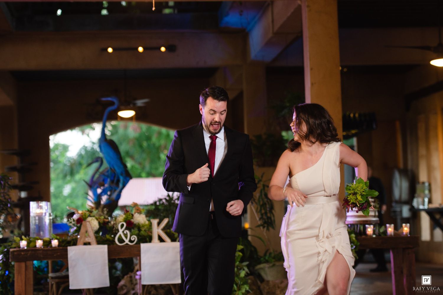 Bride and groom make grand entrance at elegant wedding reception with floral decor and monogram sign.