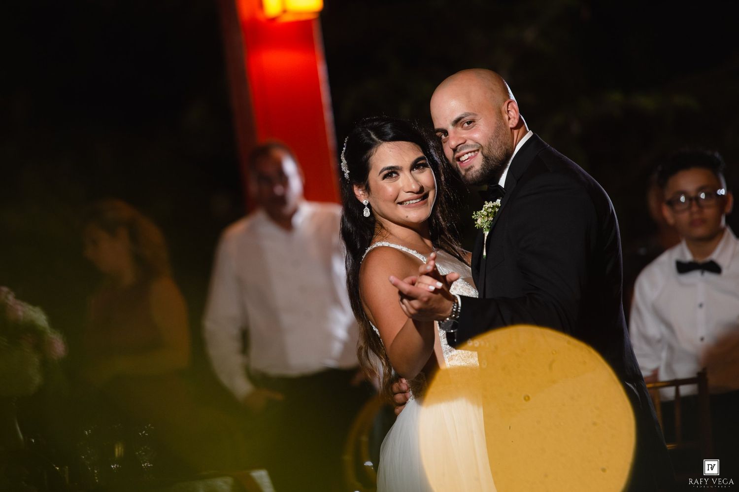 A bride and groom share a romantic dance at their wedding reception, smiling warmly under evening lights.