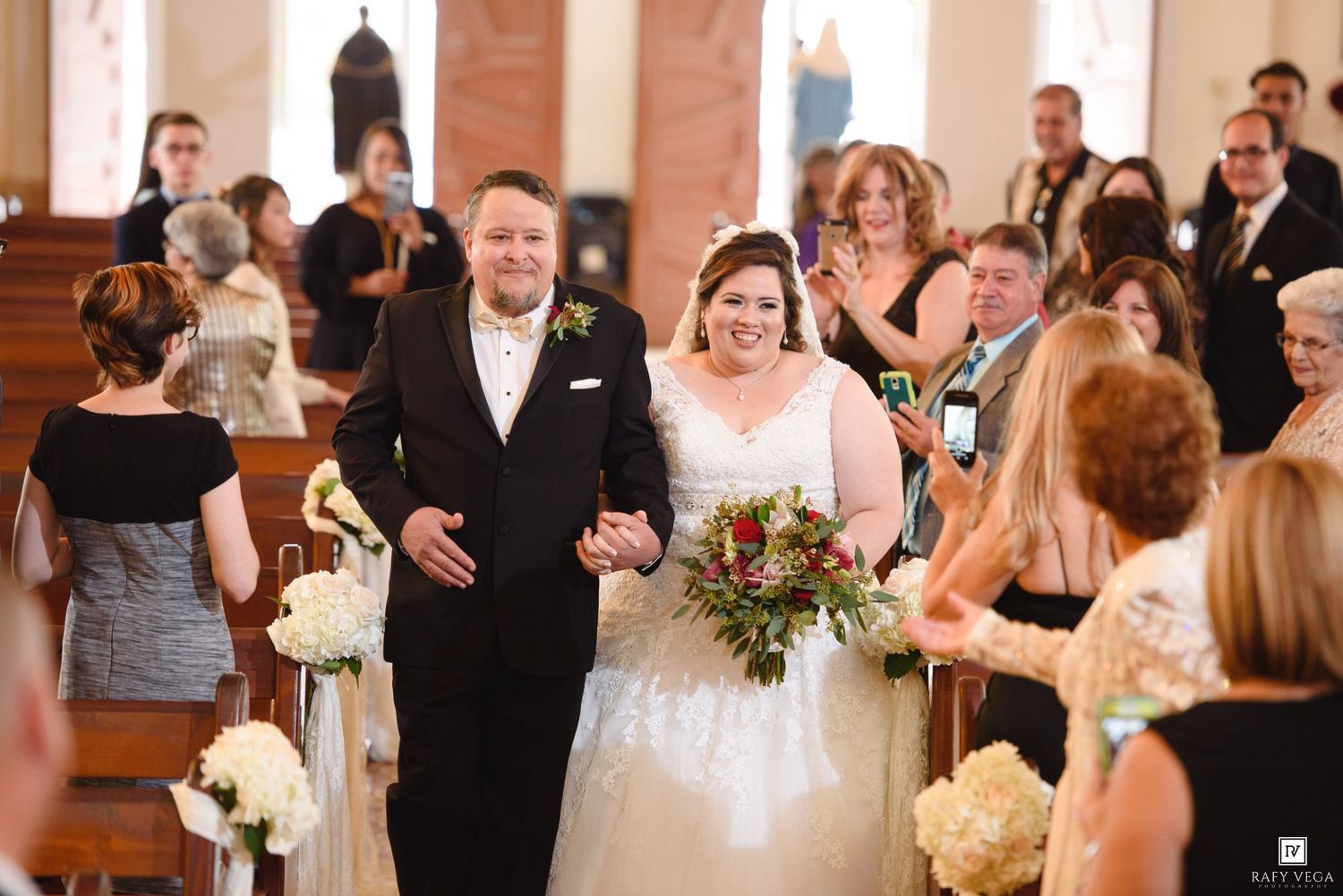 Bride and groom walk back down church aisle after wedding ceremony, bride holding colorful bouquet.