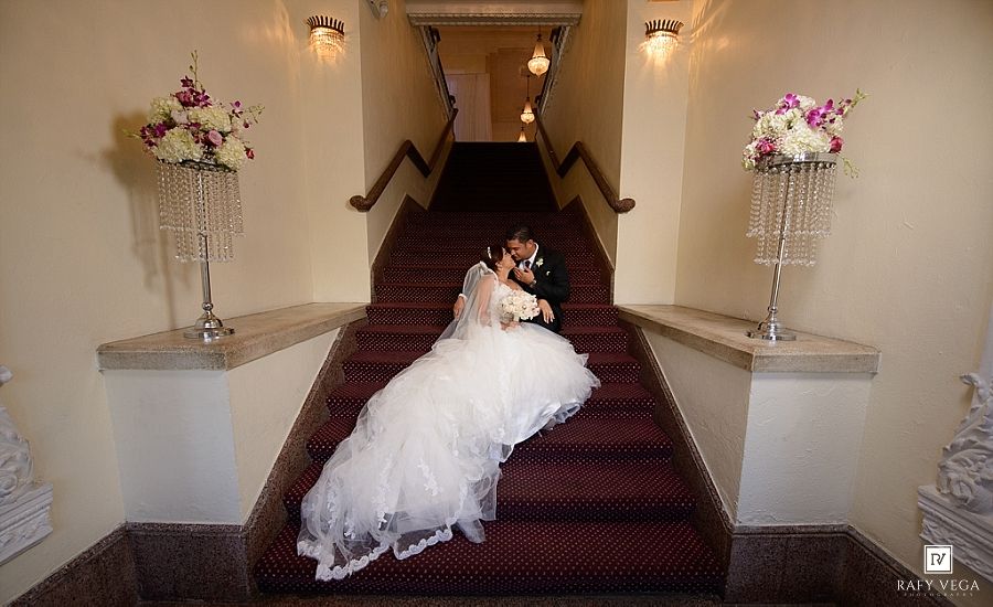 Bride and groom share a romantic kiss on elegant staircase adorned with floral arrangements at wedding venue.