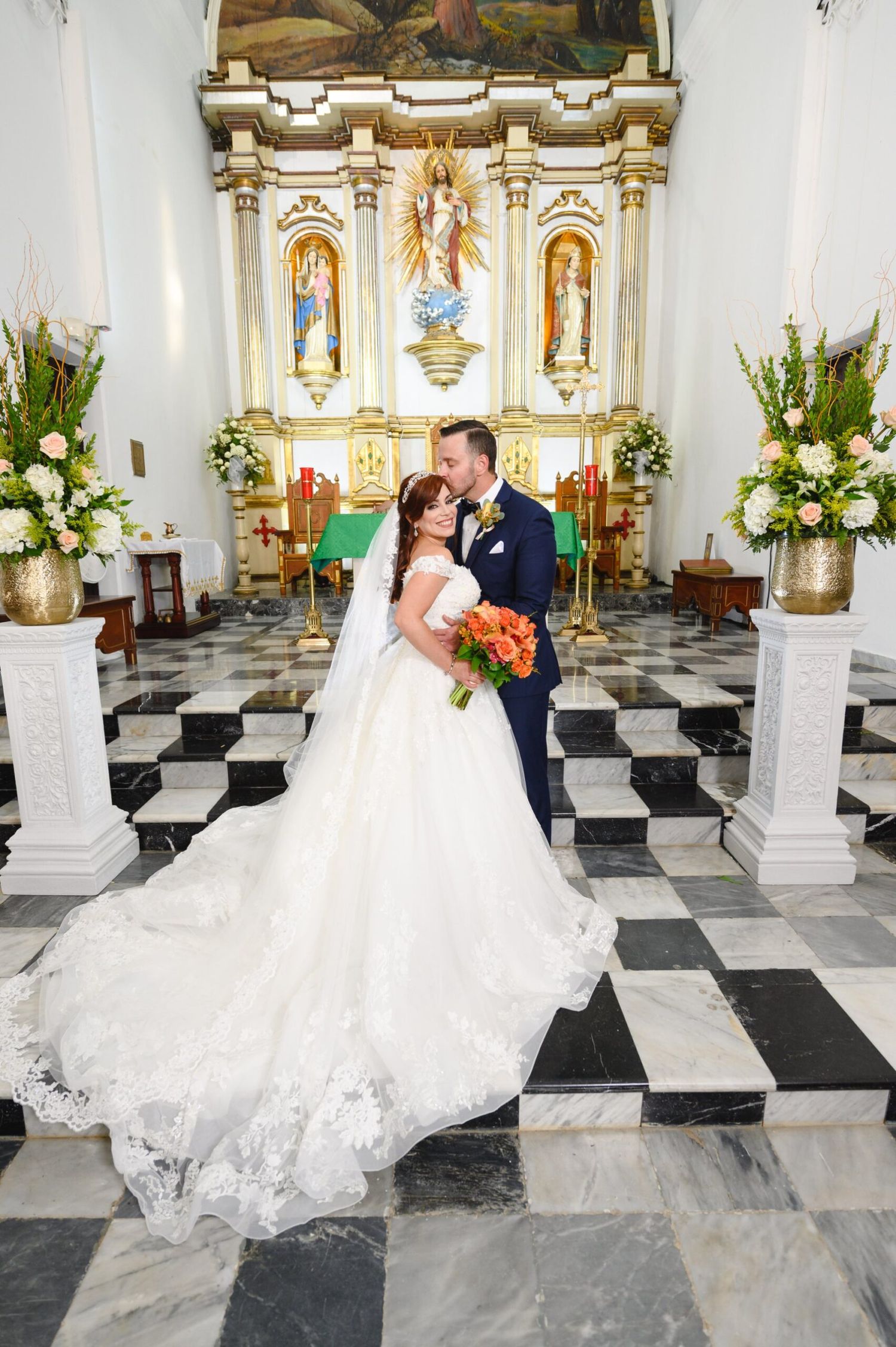 Bride and groom sharing a kiss at ornate church altar on black and white marble floor.