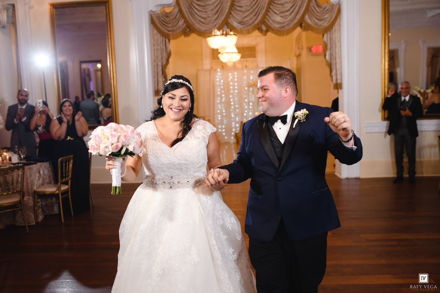 Bride and groom make grand entrance into elegant wedding reception hall, bride holding pink bouquet in white gown.