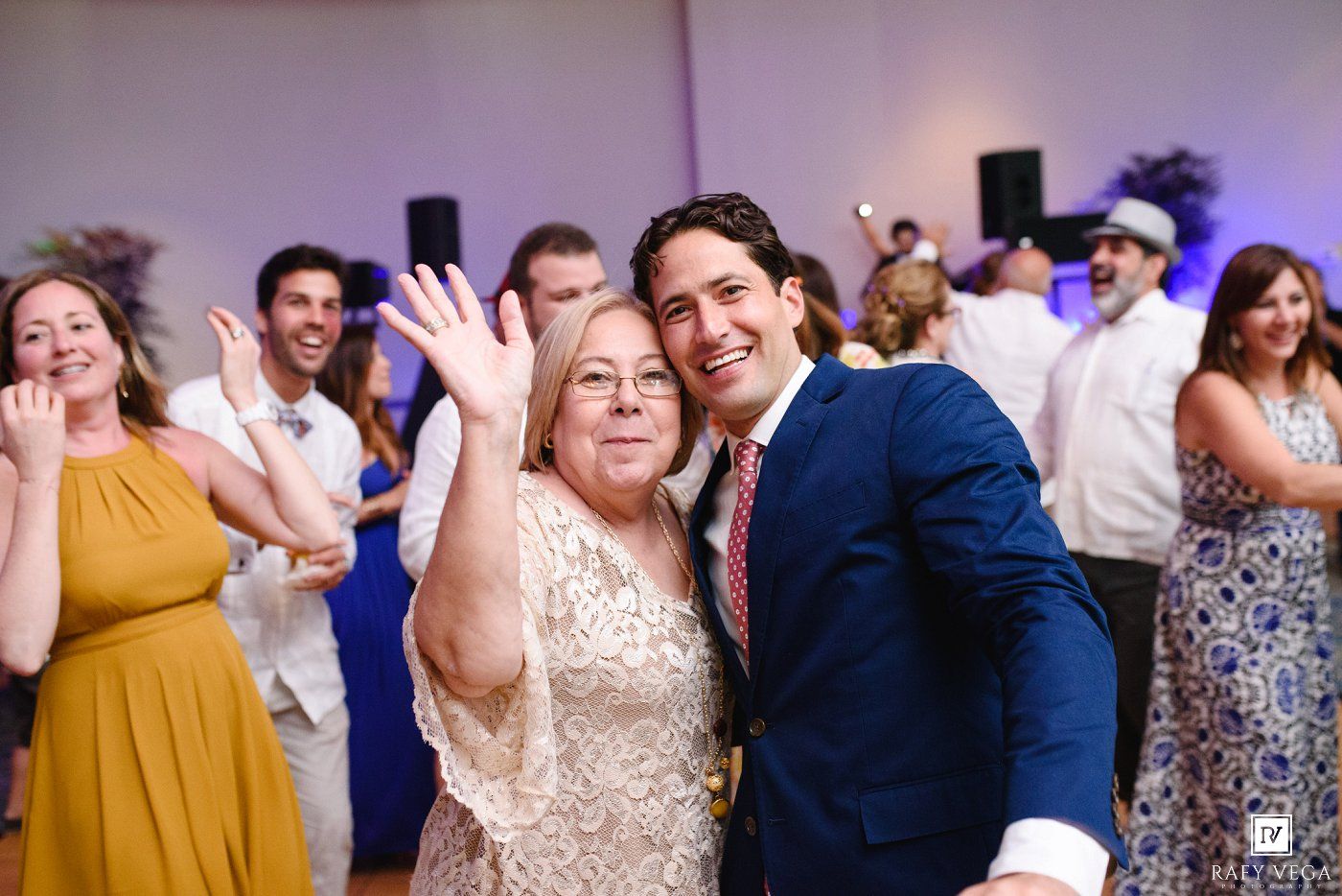 Two guests smile and dance joyfully at a lively wedding reception, surrounded by other celebrants on the dance floor.