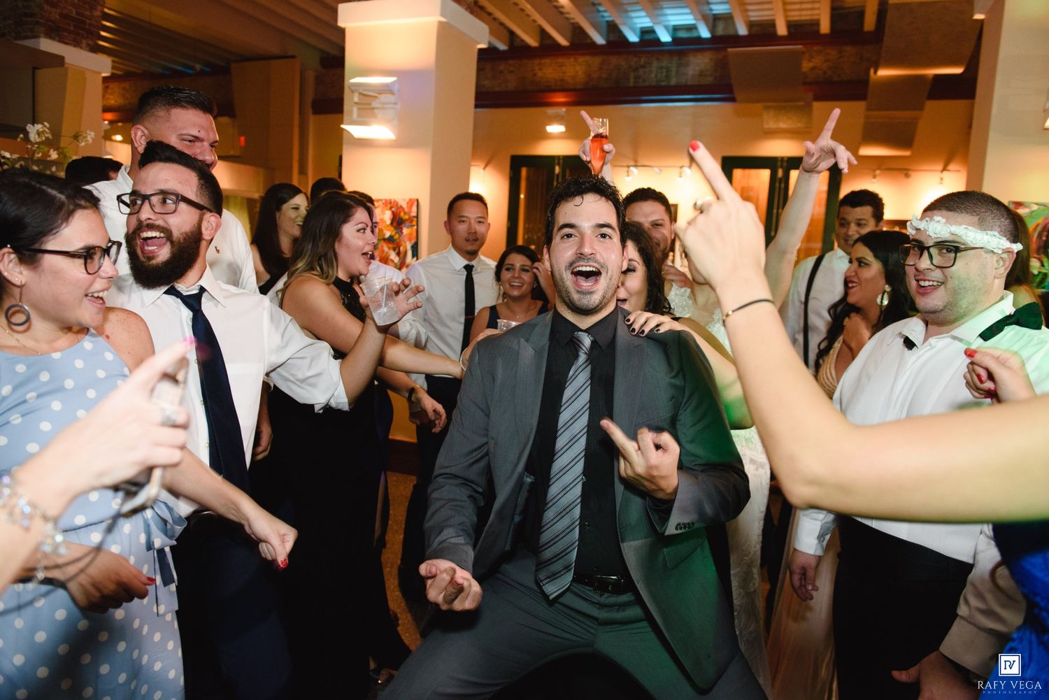 Groom dancing joyfully with wedding guests at lively indoor reception celebration.