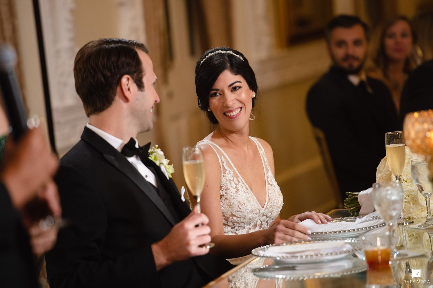 Smiling bride in lace gown toasts with champagne at elegant wedding reception dinner.