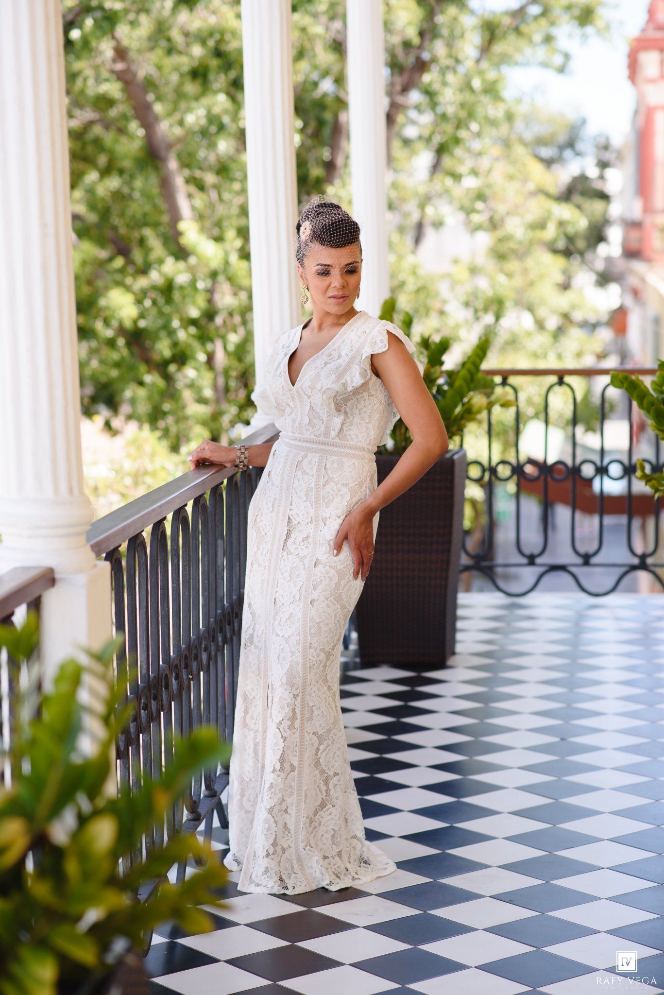 Elegant bride in white lace gown poses on a classic black and white checkered balcony with ornate railings.