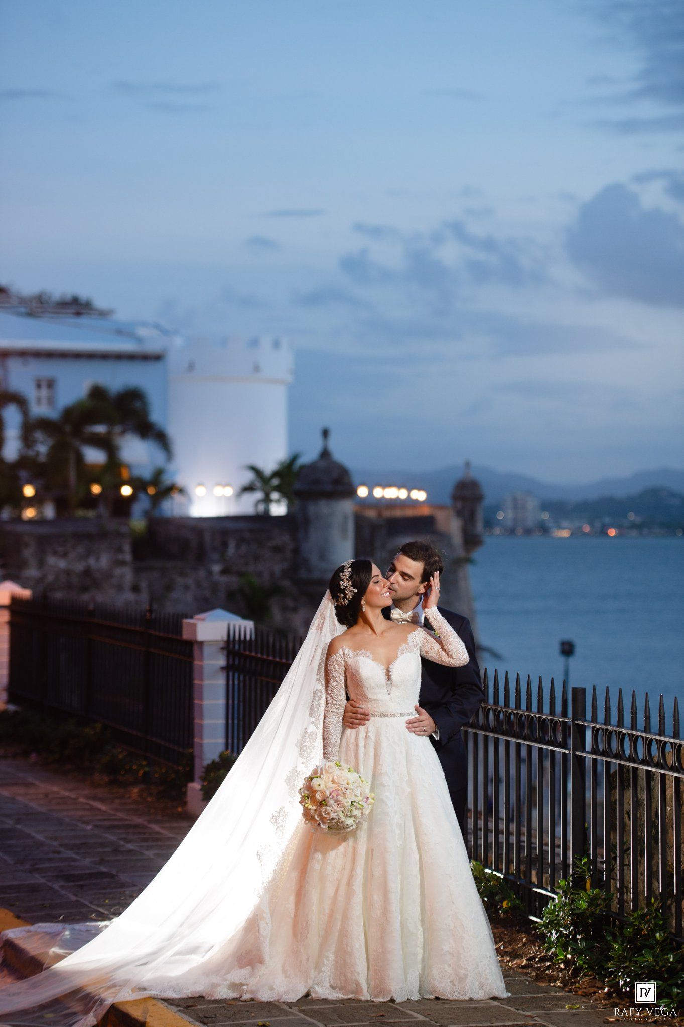 Bride and groom share a romantic kiss at dusk with a waterfront fortress backdrop in Old San Juan, Puerto Rico.