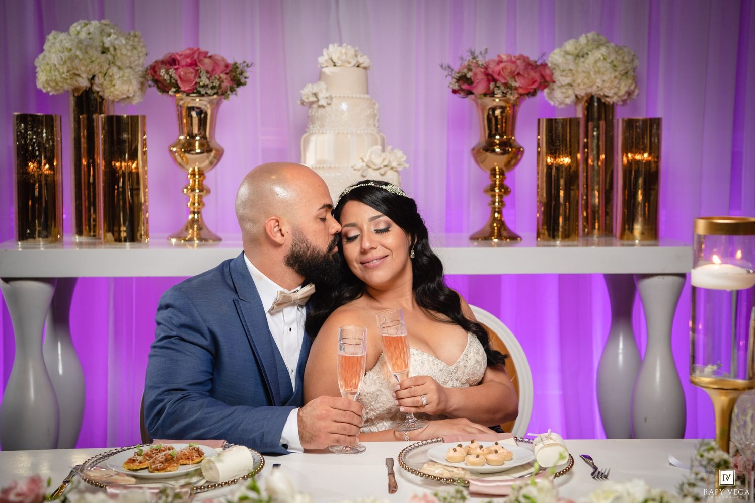 Bride and groom share a romantic moment at their wedding reception table with champagne flutes and elegant floral decor.