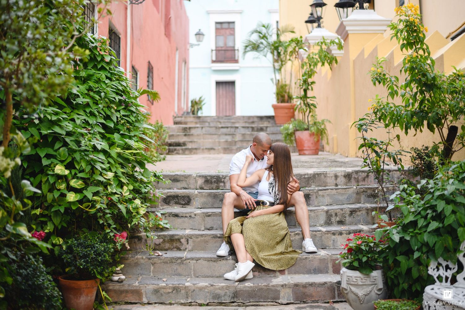 Couple sharing a romantic kiss on colorful colonial steps surrounded by lush greenery in Old San Juan.