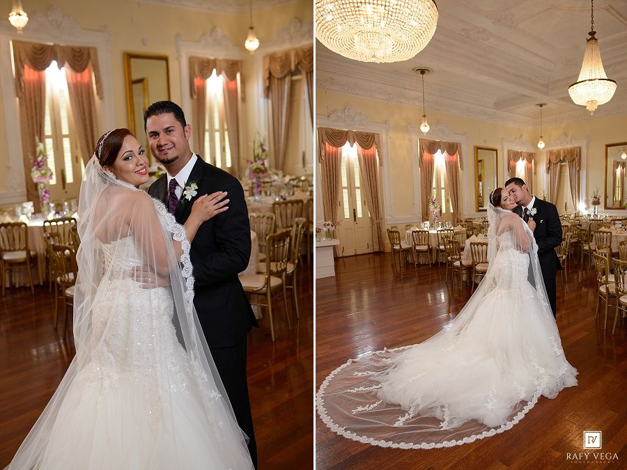 Elegant bride and groom pose in ornate ballroom, bride wearing lace mermaid gown with cathedral veil.