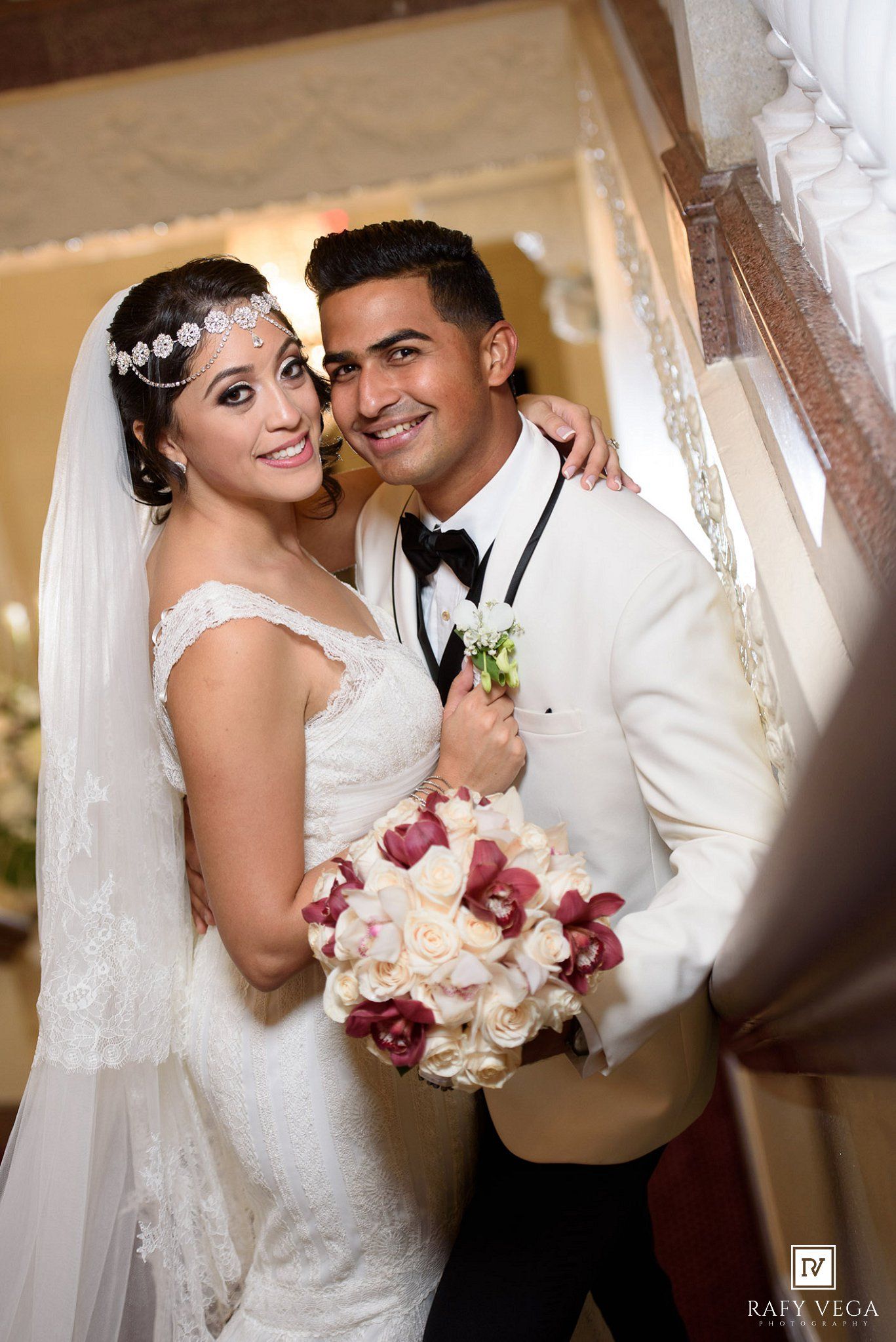 Bride and groom posing together on their wedding day, bride holding a bouquet of white and red flowers.