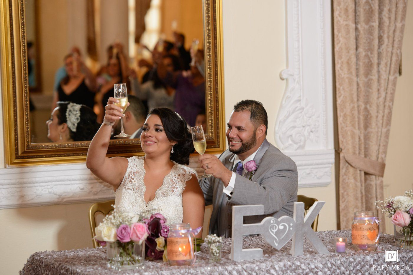 Bride and groom raise champagne glasses in a toast at their elegant wedding reception sweetheart table.