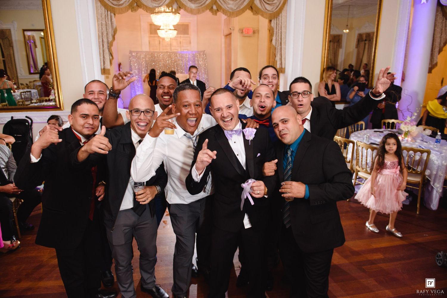 Groom posing with groomsmen and guests at festive wedding reception celebration.