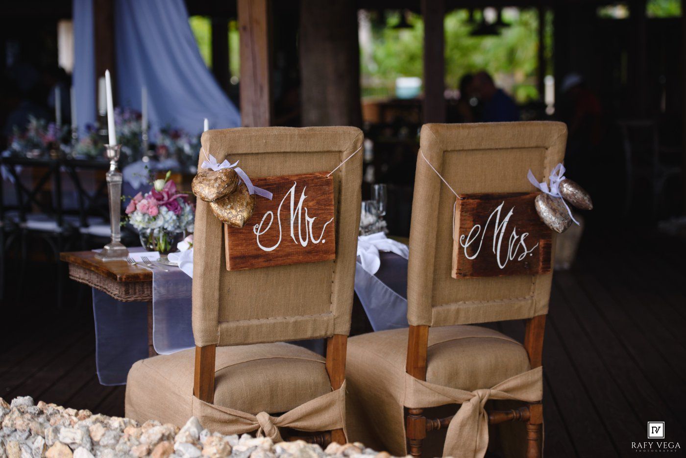 Mr. and Mrs. wooden signs hanging on burlap-decorated wedding reception chairs at an elegant outdoor venue.