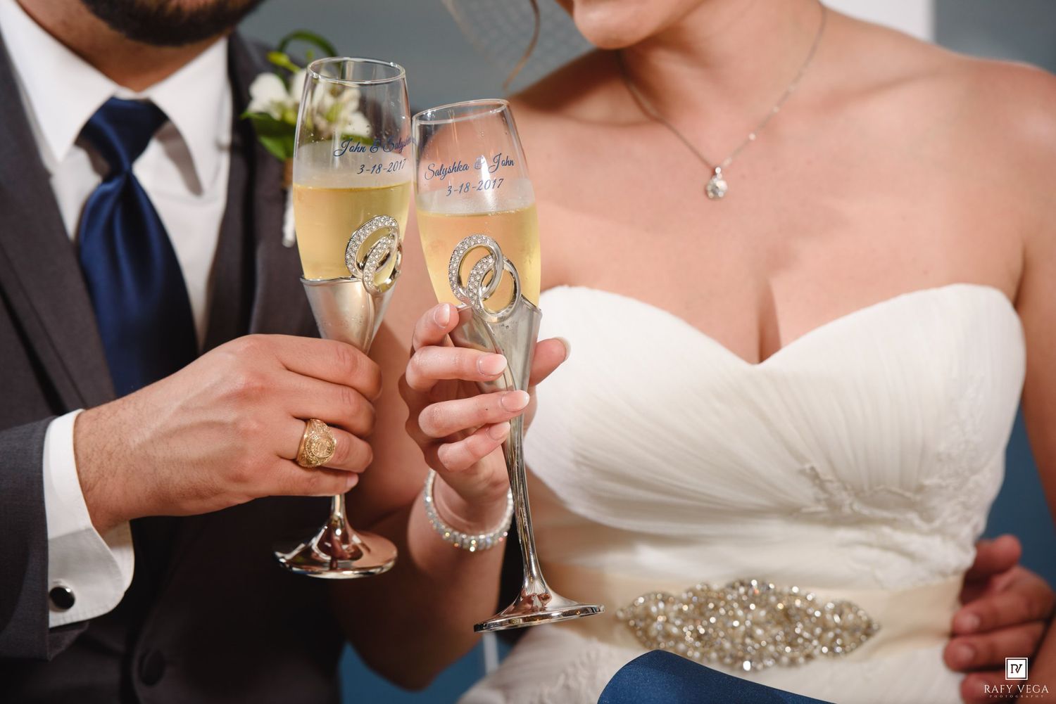 Newlywed couple toasting with elegant champagne flutes adorned with rings at their wedding reception.
