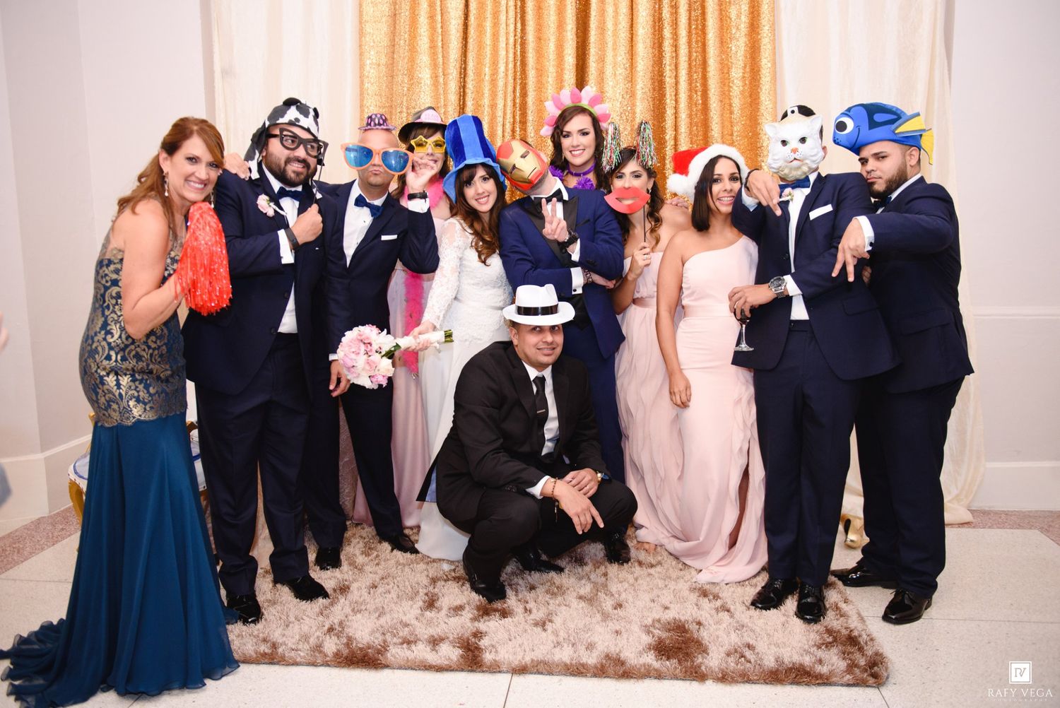 Wedding party posing with fun photo booth props including hats and masks at a formal reception.