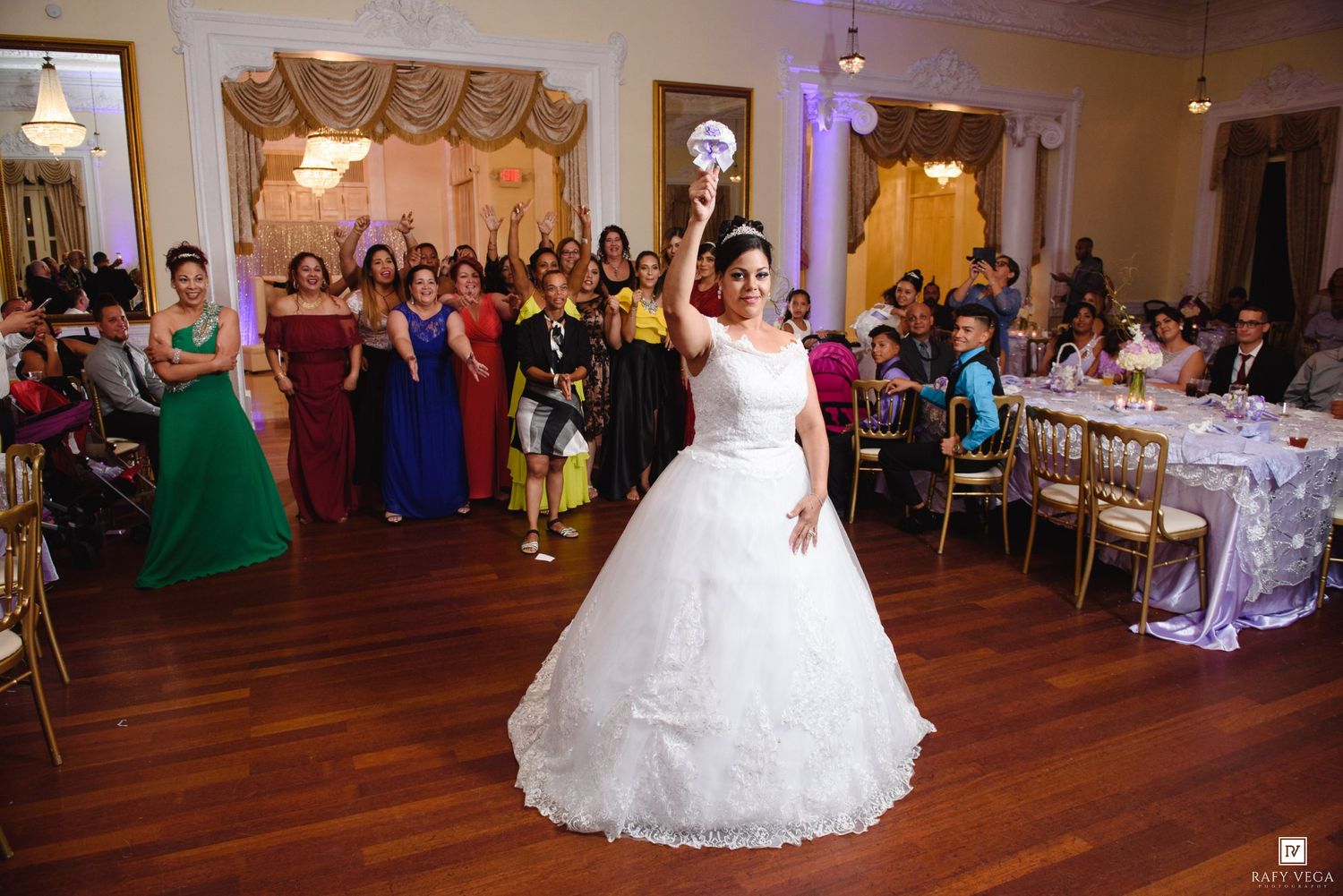 Bride in white ball gown tosses bouquet to guests at wedding reception.