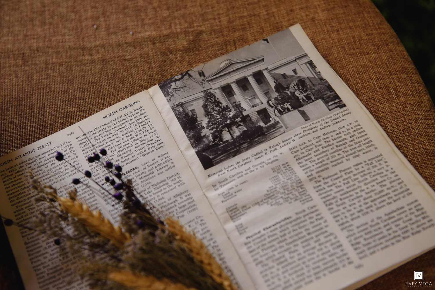 Open vintage book with black-and-white photo, dried wheat and berry stems on burlap background.