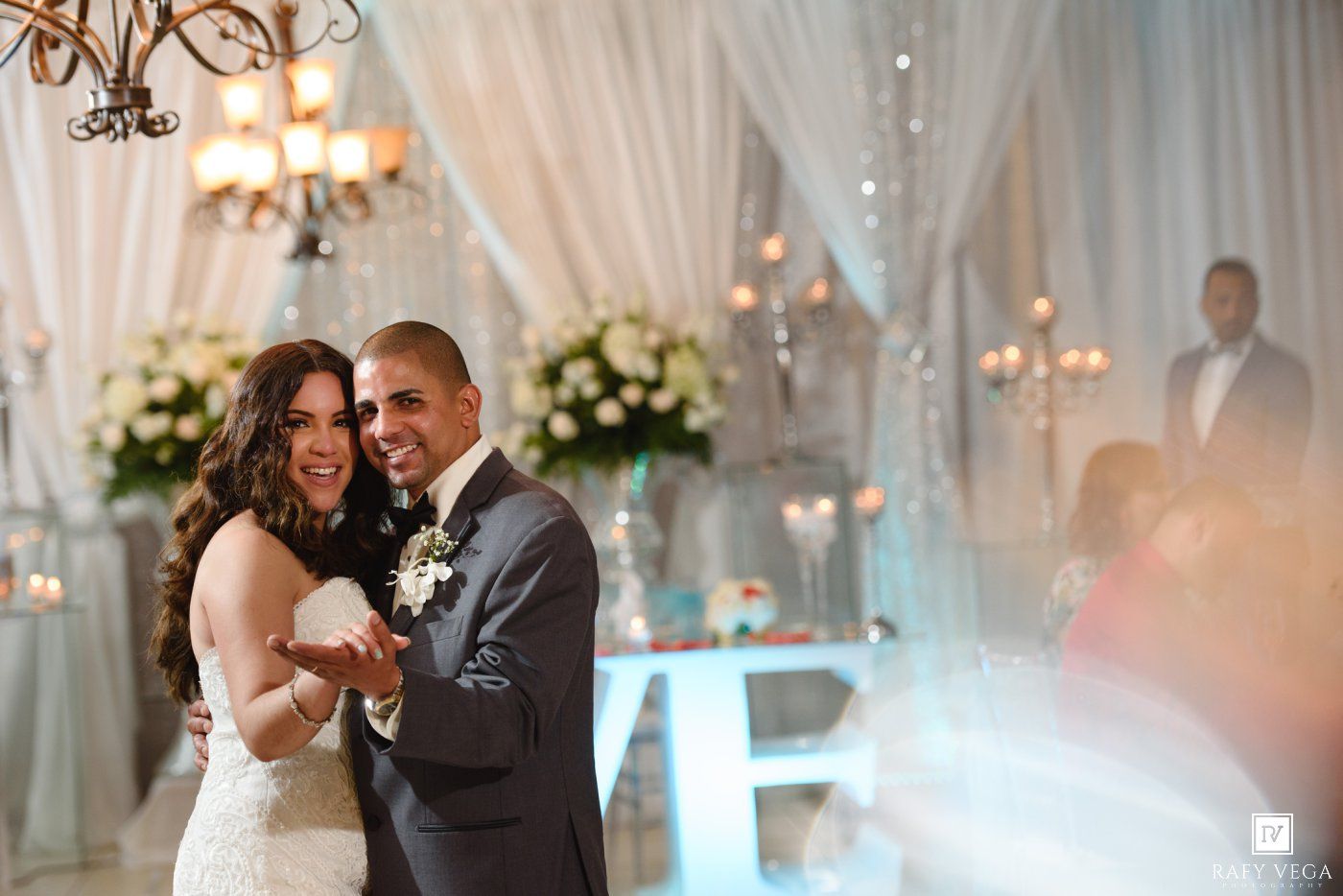 Happy bride and groom smiling together on wedding dance floor with white draping and floral decor in background.