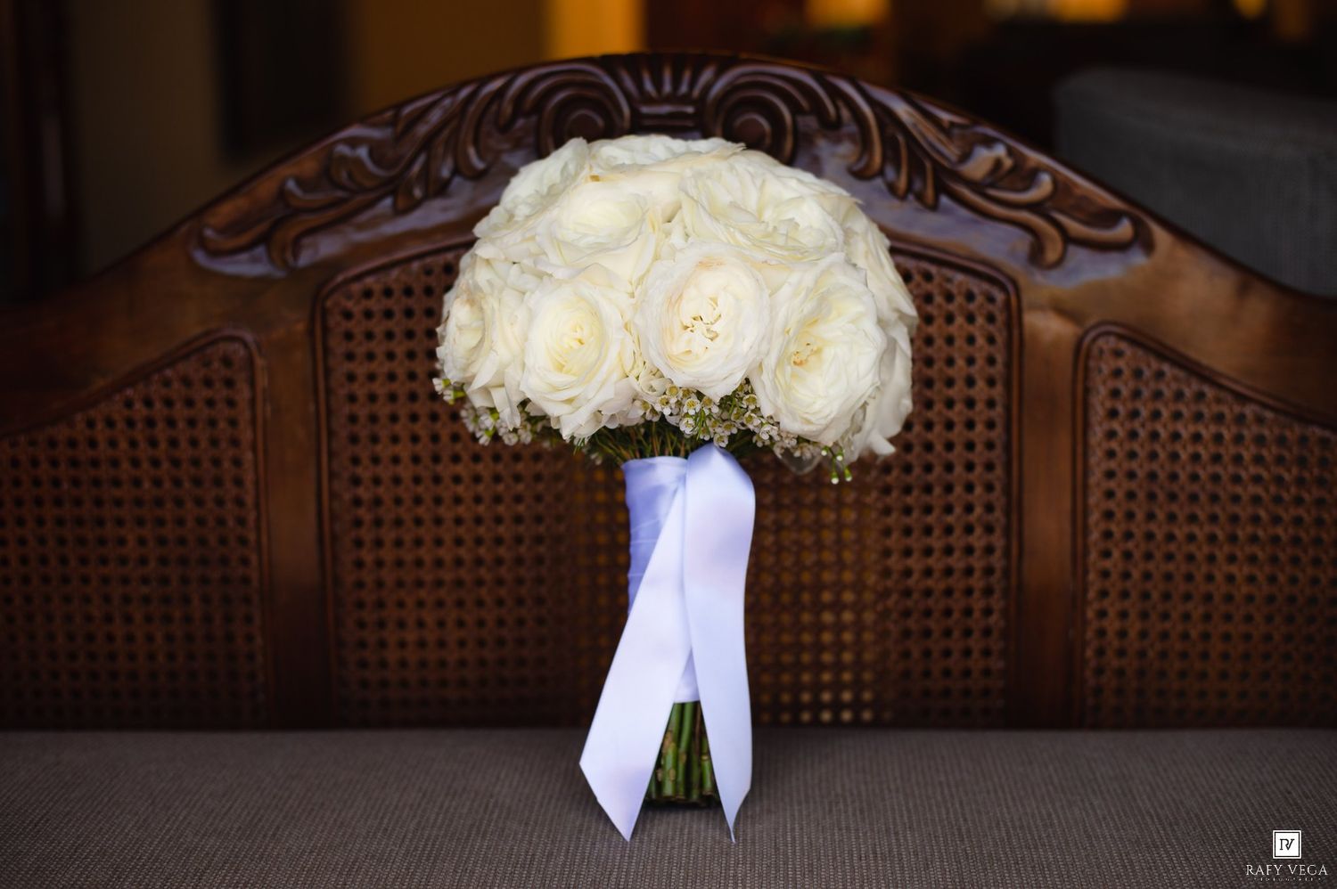 White rose bridal bouquet with baby's breath and white ribbon resting against a carved wooden headboard.