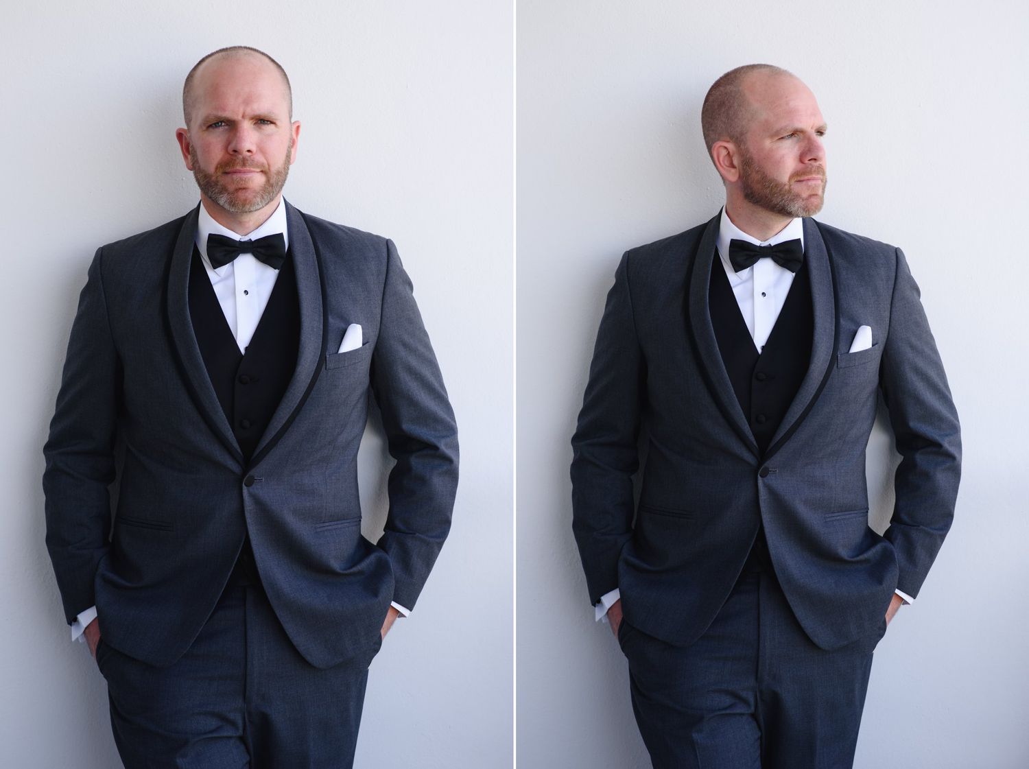 Bald man in dark charcoal tuxedo with black bow tie and white pocket square posing confidently against white wall.