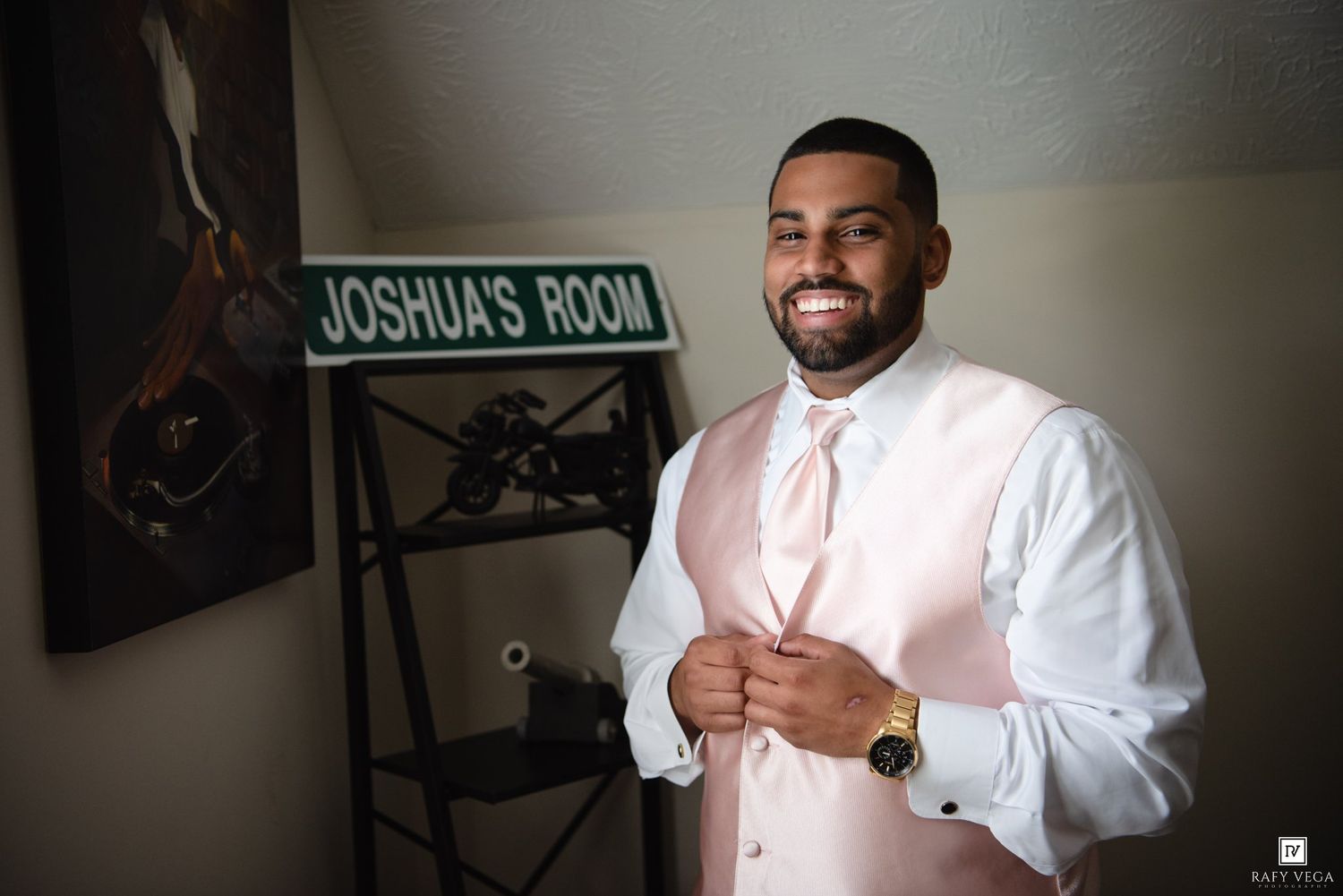 Smiling groom in pink vest and white shirt adjusting his vest in Joshua's Room before his wedding ceremony.