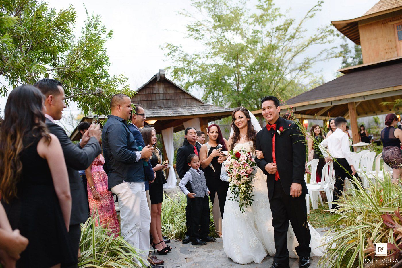 Bride and groom walk down the aisle at an outdoor wedding ceremony surrounded by smiling guests.