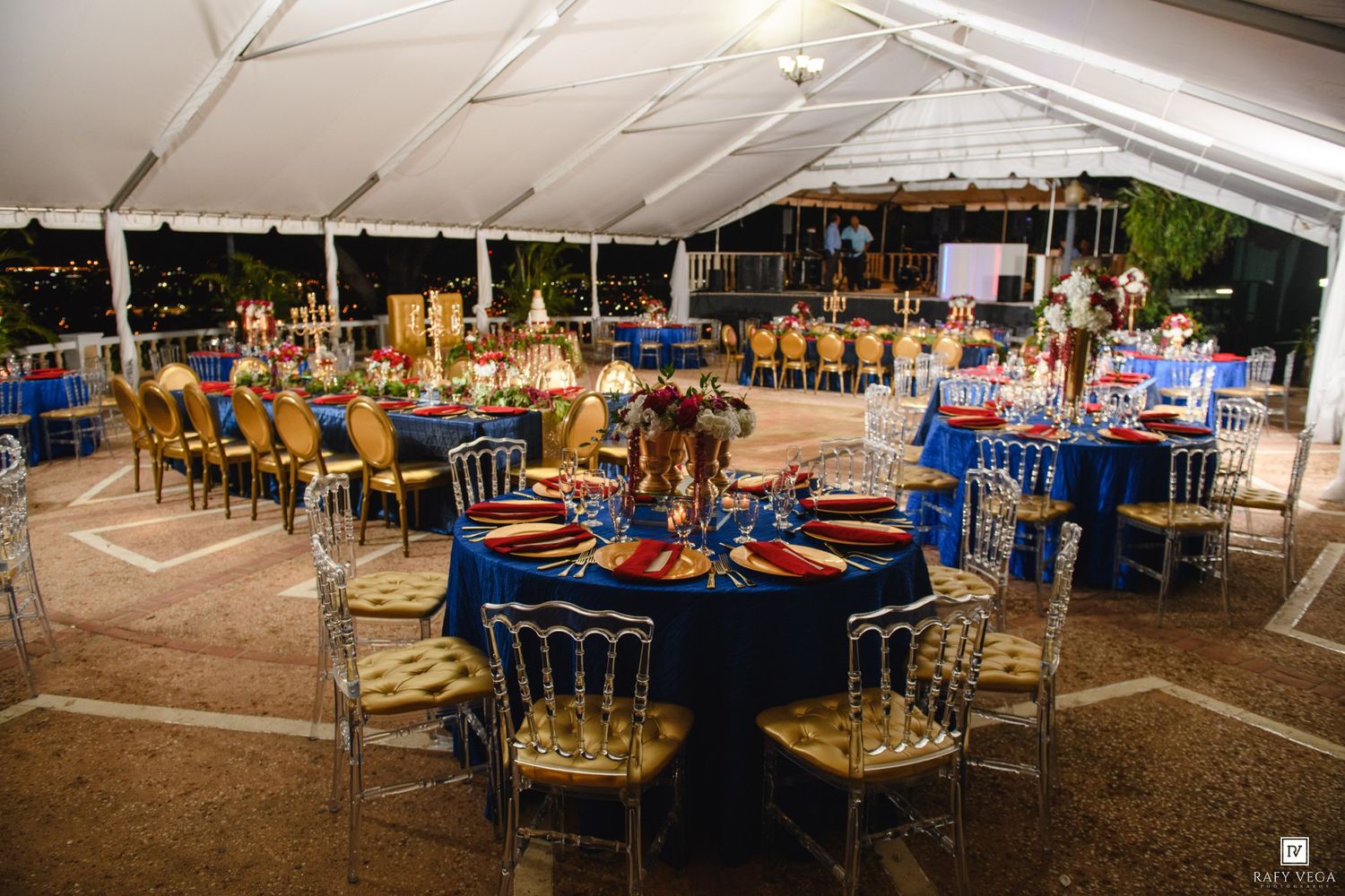 Elegant outdoor event tent with royal blue tablecloths and gold chairs set for a formal banquet dinner.