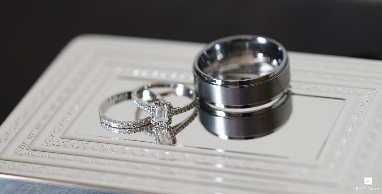 Diamond engagement ring and two silver wedding bands displayed on a white decorative tray.