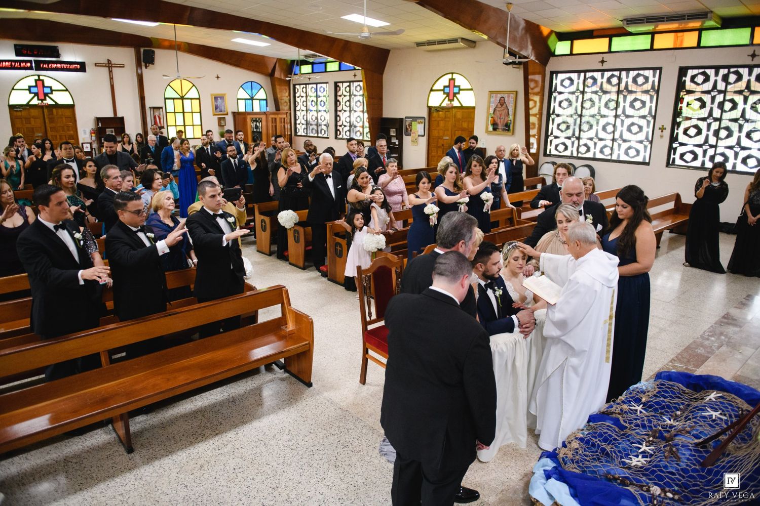 Wedding ceremony in church with guests standing in pews as officiant performs the marriage ritual.