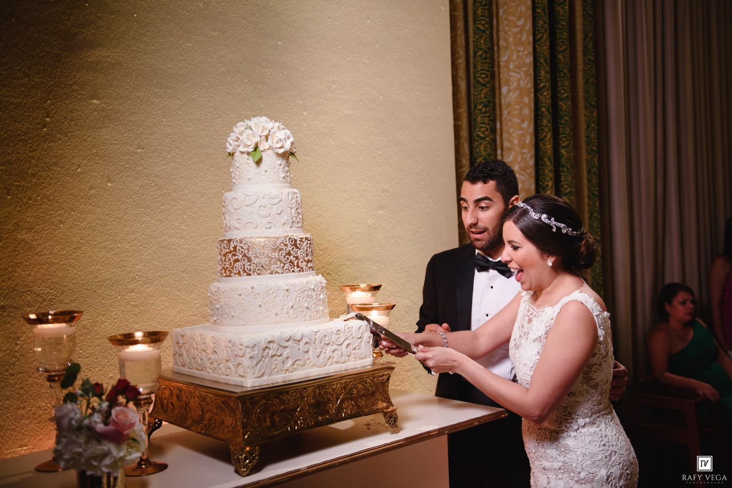 Bride and groom cutting a tall white tiered wedding cake at their elegant reception venue.