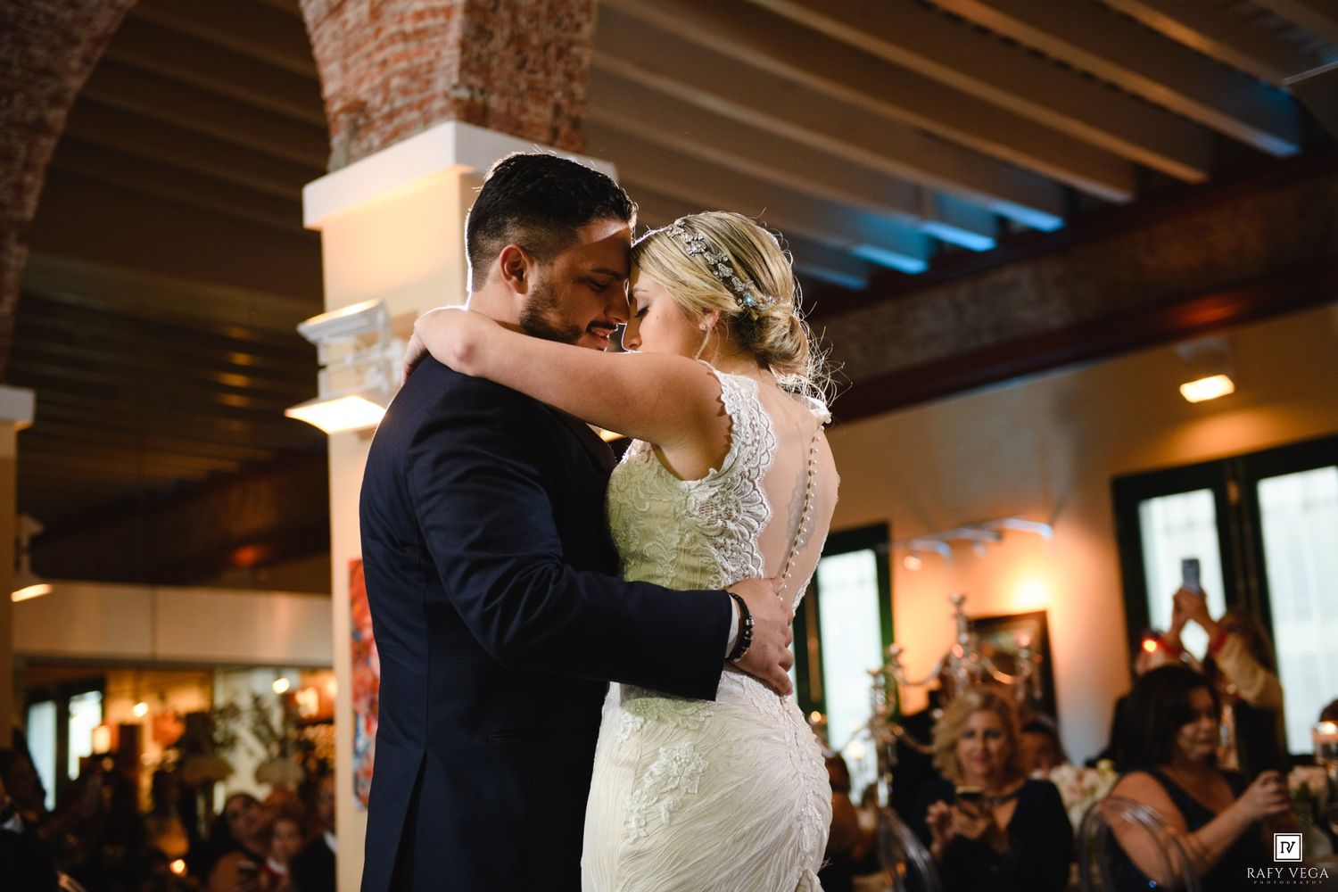 Bride and groom share their first dance at a warmly lit wedding reception venue.