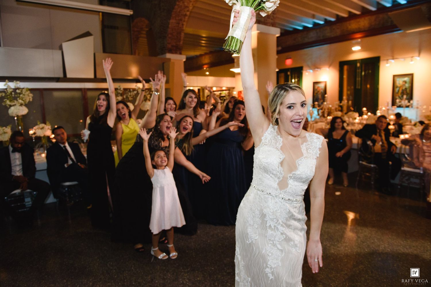 Bride tosses bouquet to excited wedding guests during reception celebration.