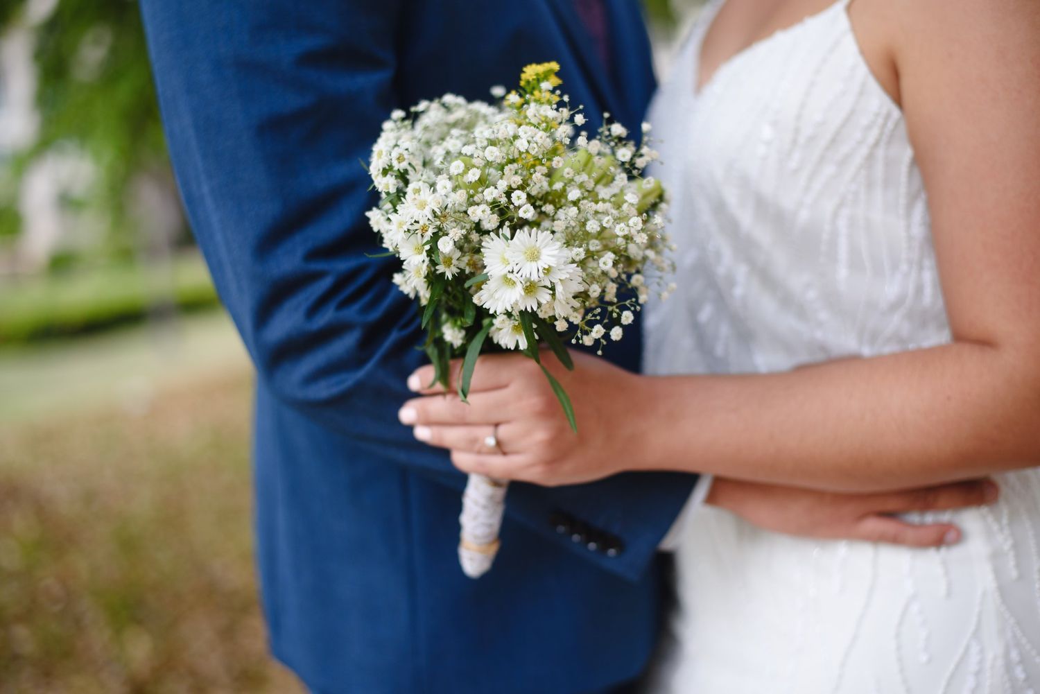 Bride holding a white baby's breath bouquet beside groom in blue suit at outdoor wedding ceremony.