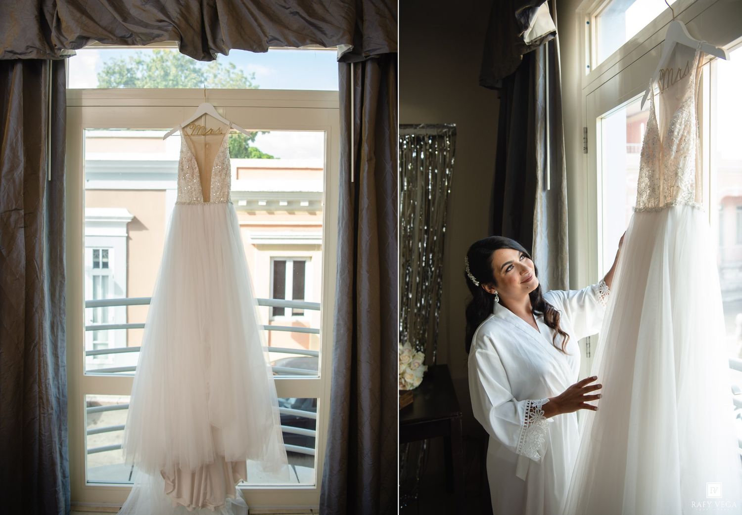 Bride in white robe admiring her elegant wedding gown hanging by a sunlit window on her wedding day.