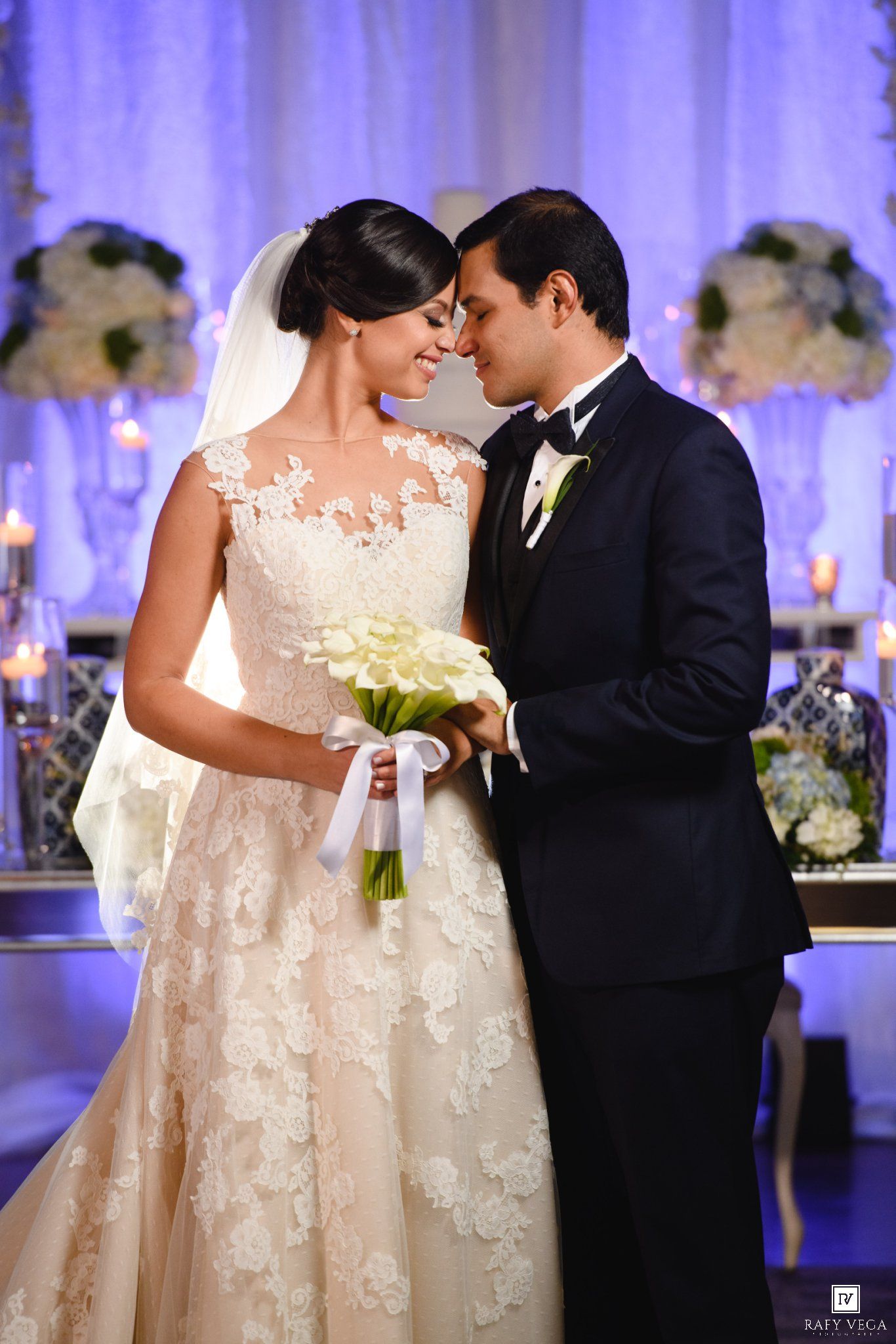 Bride and groom share romantic moment at elegant wedding reception, bride holding white calla lily bouquet in lace gown.