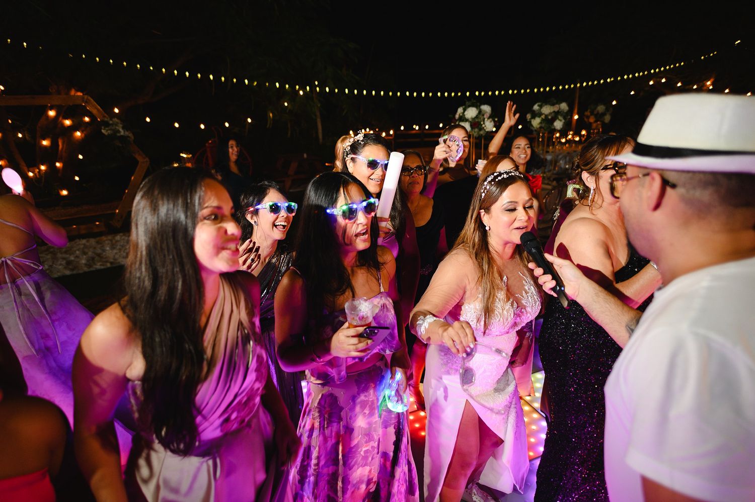 Women in pink outfits dancing at a festive outdoor night party with string lights.