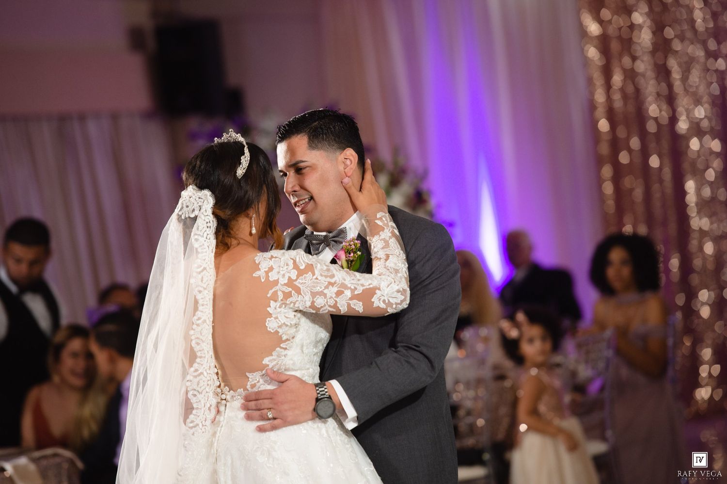 Bride and groom share romantic first dance in decorated wedding reception venue with pink uplighting.