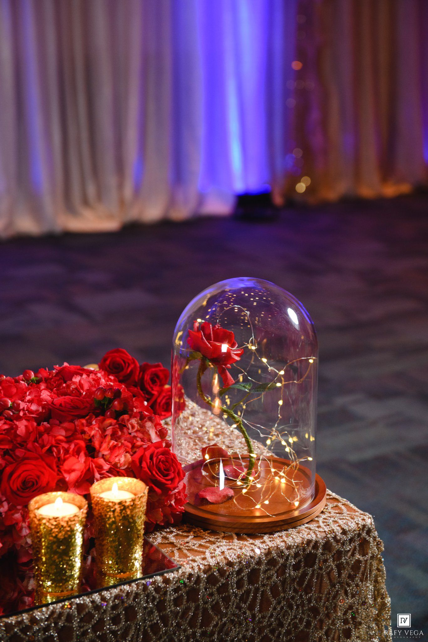 Enchanted Beauty and the Beast wedding centerpiece with red rose under glass dome, fairy lights, and gold candles.