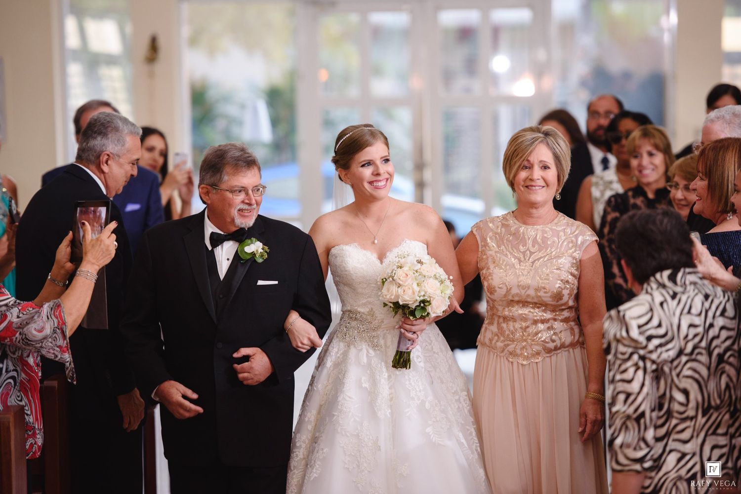 Bride walks down the aisle with parents during elegant wedding ceremony procession.