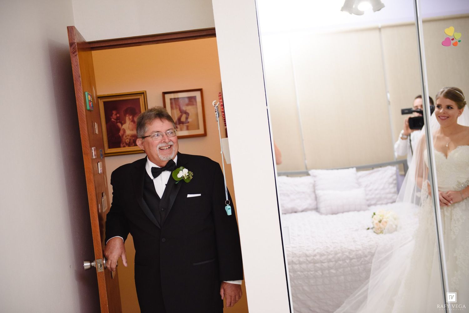 Elderly man in tuxedo sees bride in wedding dress reflected in mirror during emotional first look moment.