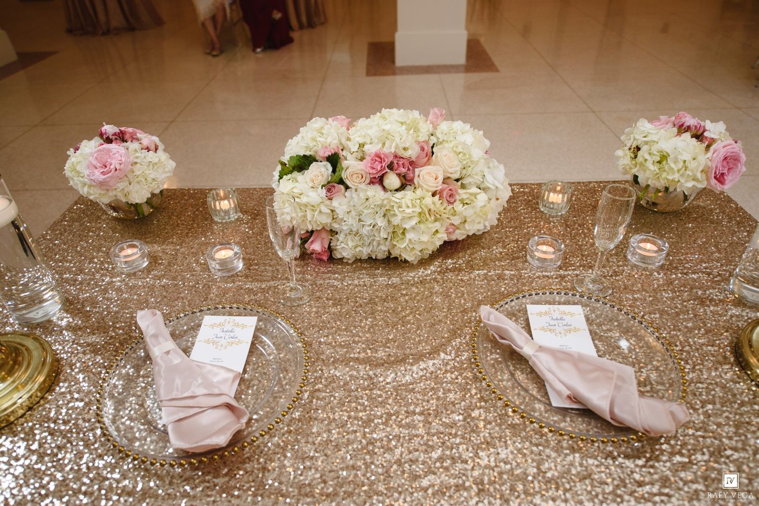Gold sequin sweetheart table adorned with white hydrangea and pink rose floral centerpieces.