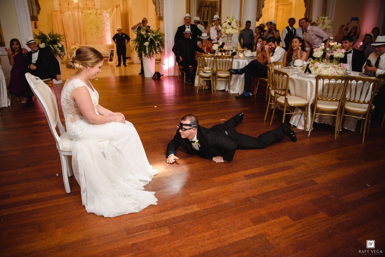 A wedding guest dramatically slides across the dance floor entertaining the bride seated in a chair during the reception.