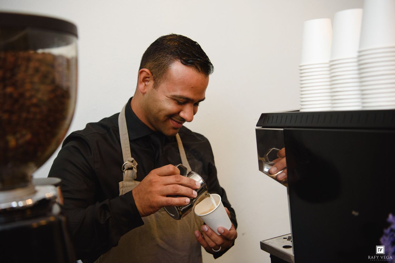 Smiling barista preparing a latte in a modern coffee shop with espresso equipment.