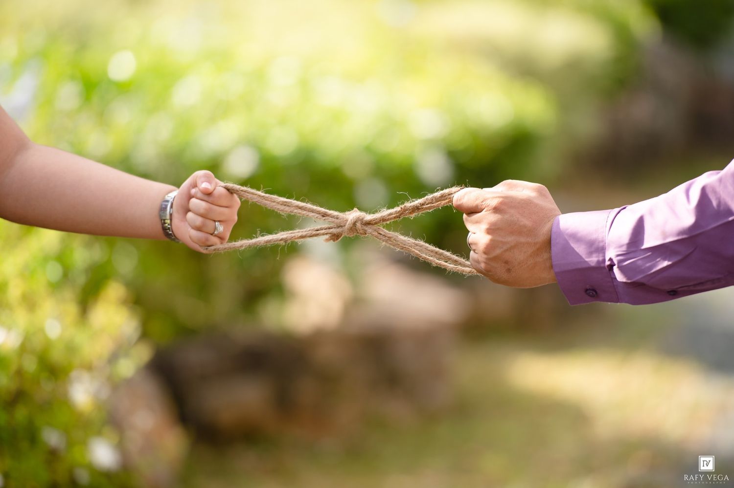 Two hands pulling opposite ends of a twisted rope knot symbolizing connection and unity in an outdoor setting.