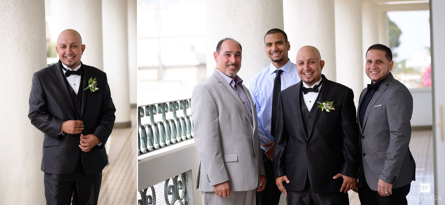 Group of groomsmen in suits and bow ties posing together at an elegant wedding venue with white columns.
