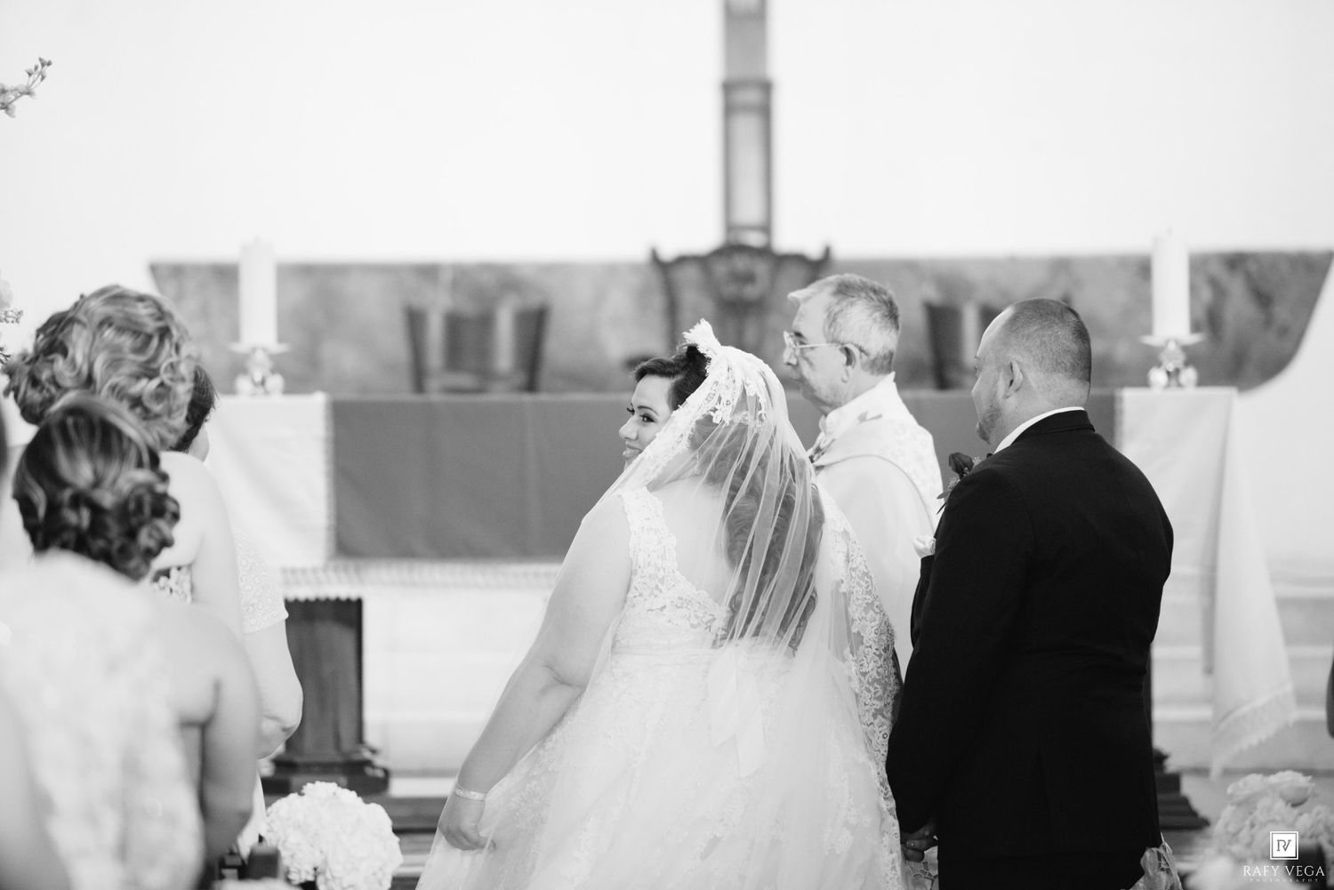 Black and white photo of a bride and groom exchanging vows at a church altar during their wedding ceremony.