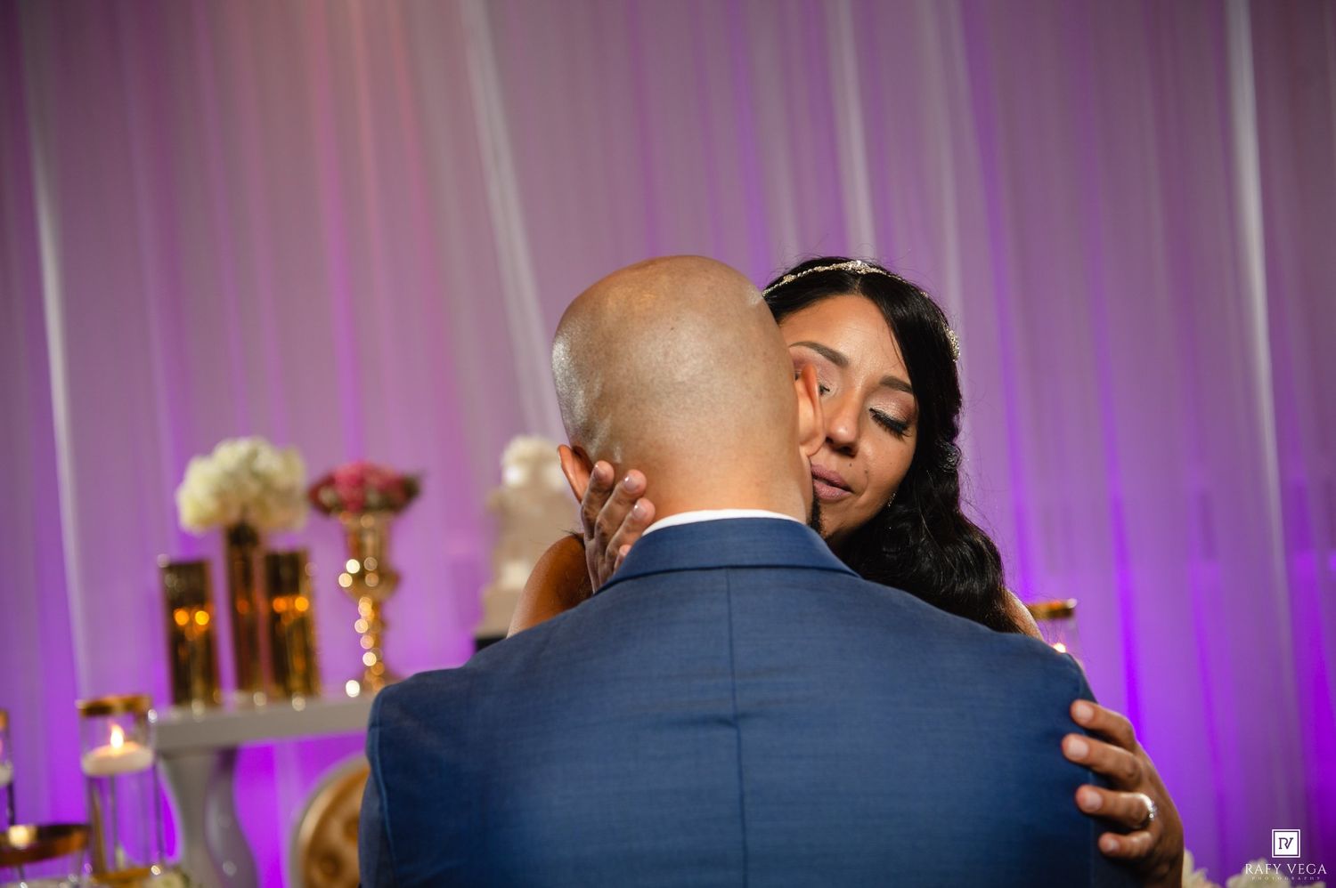 Bride and groom share an emotional first dance embrace at a wedding reception with purple uplighting.