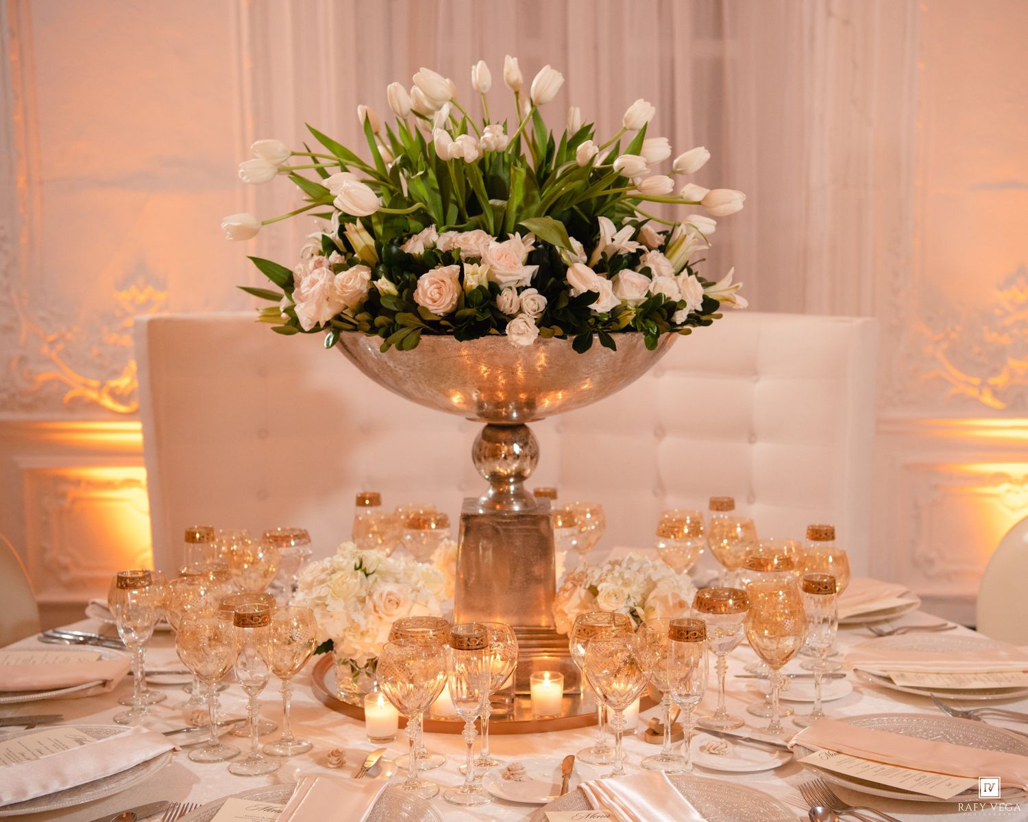 Elegant wedding reception table with tall silver floral centerpiece of white tulips, candles, and crystal glassware.